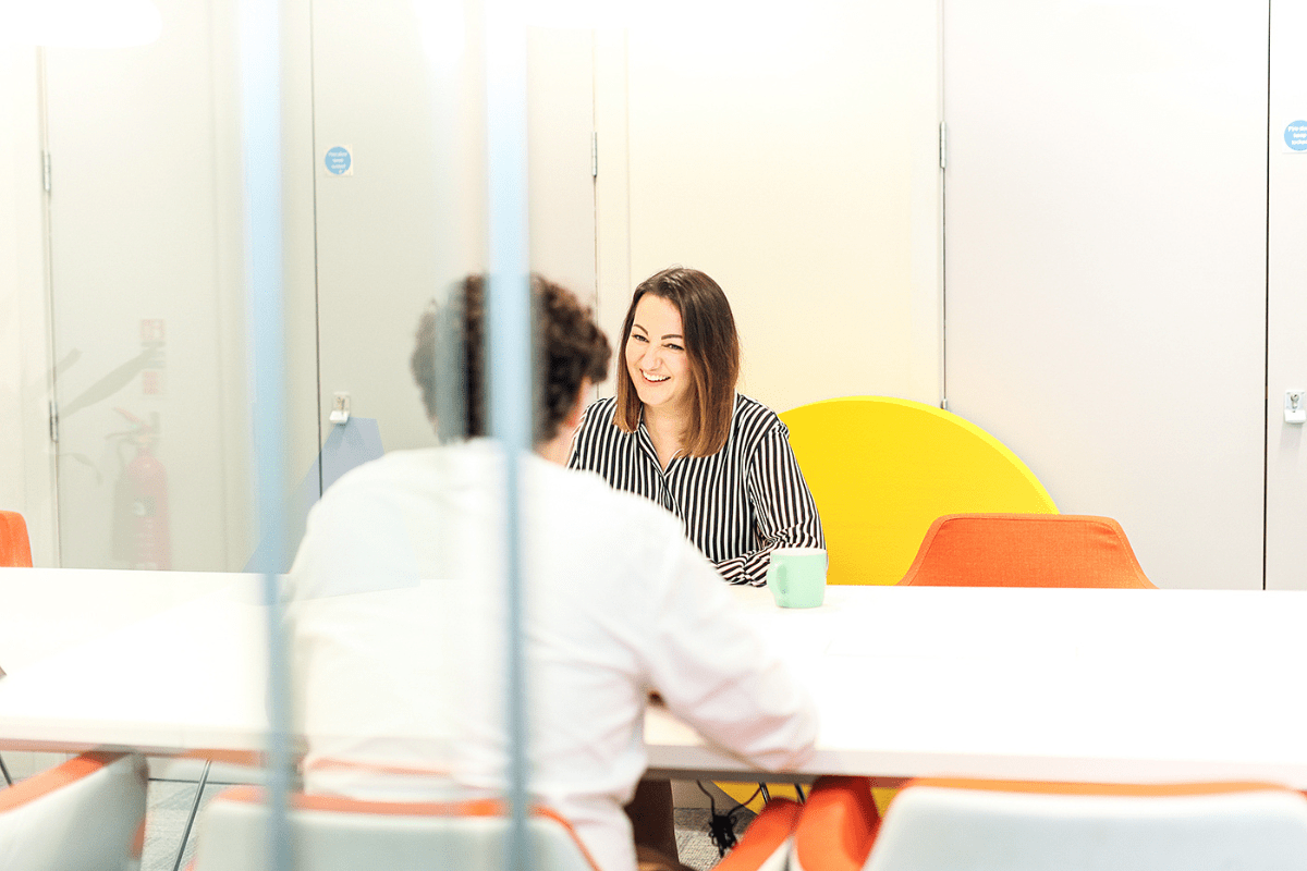 A man and woman sit at a boardroom table discussing new hires and how to help business owners and hiring managers find the right fit